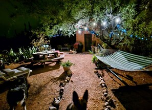 An outdoor patio area with a wooden table, chairs, a hammock, and string lights. - Knightly's Ranch Guesthouse  (Tucson)