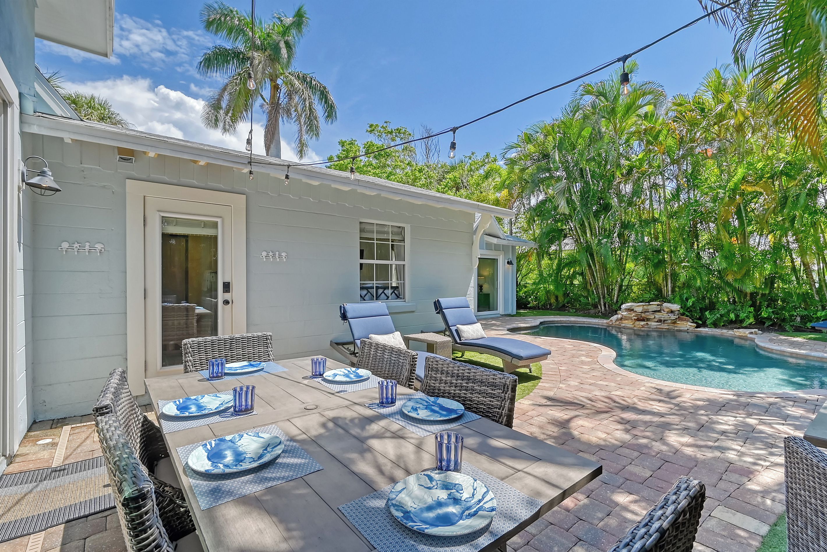 A patio with a pool, outdoor furniture, and a dining table set for four.