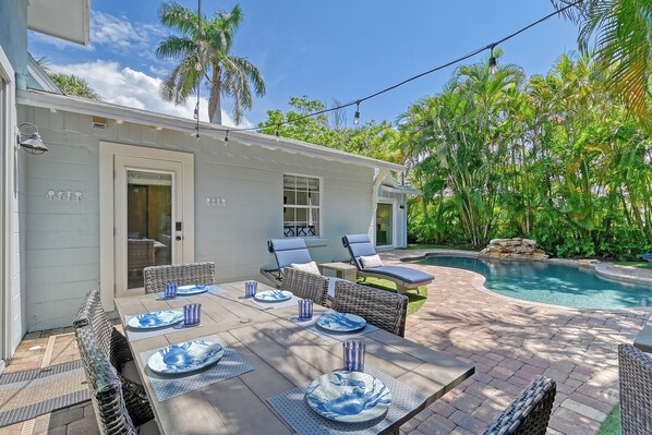A patio with a pool, outdoor furniture, and a dining table set for four.