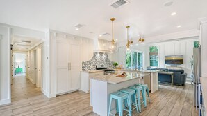 Een moderne keuken met een centraal eiland, blauwe barkrukken en hanglampen.