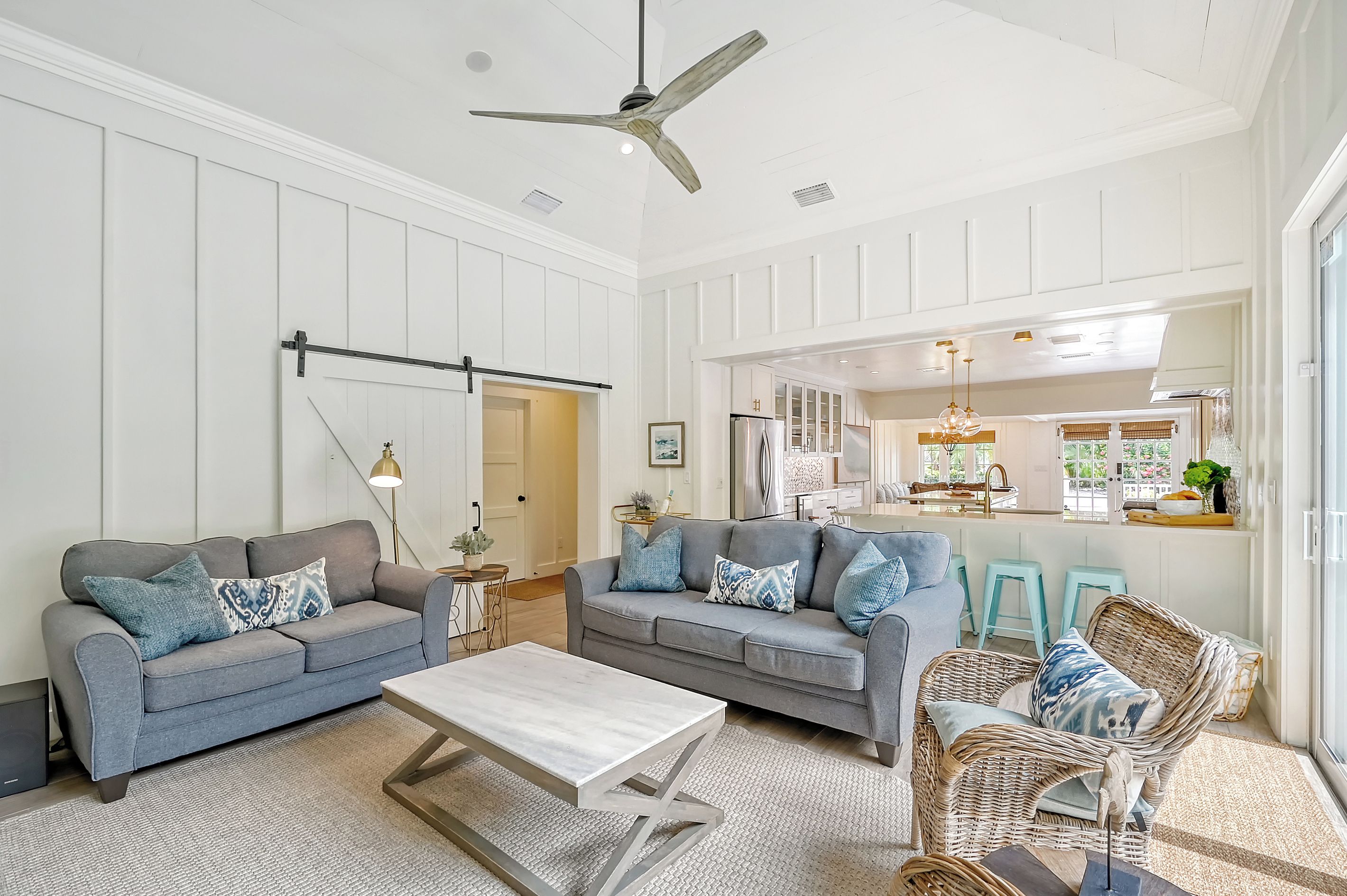 A spacious living room with two grey sofas, a coffee table, a wicker chair, and a ceiling fan.