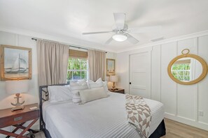 A bedroom with a bed, a nightstand, a lamp, a ceiling fan, and a window with curtains. - Unwind Sunshine | Heated Pool | 1.5 Blocks to Beach | Complimentary Bikes (Holmes Beach)