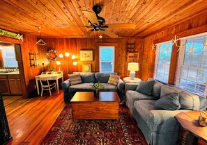 Ein gemütliches Blockhaus-Interieur mit Holzbalkendecke, zwei Sofas, einem Couchtisch, einem Esstisch und einer Küchenzeile.