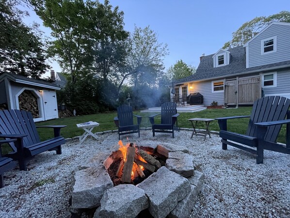 A backyard with a fire pit surrounded by Adirondack chairs, a grill, and a shed. - Private Beach Access, Great Family Get Away. (Brewster)