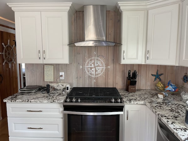 A kitchen with white cabinetry, a stainless steel range hood, a built-in oven, and a granite countertop.