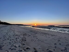 A beach with footprints leading to the water, a sunset in the background, and a clear sky. - Private Beach Access, Great Family Get Away. (Brewster)