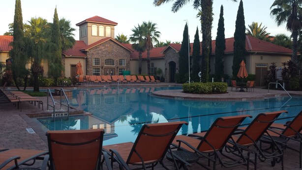 A swimming pool with lounge chairs and a building with a red roof in the background. - 2 Bed/2 Bath Resort Condo near Disney. (Davenport)