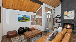 A spacious living room with a fireplace, wooden ceiling beams, a large TV, and a cozy seating area.