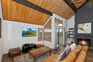 Un salon spacieux doté d’une cheminée, de poutres apparentes en bois, d’un grand téléviseur et d’un coin salon confortable.
