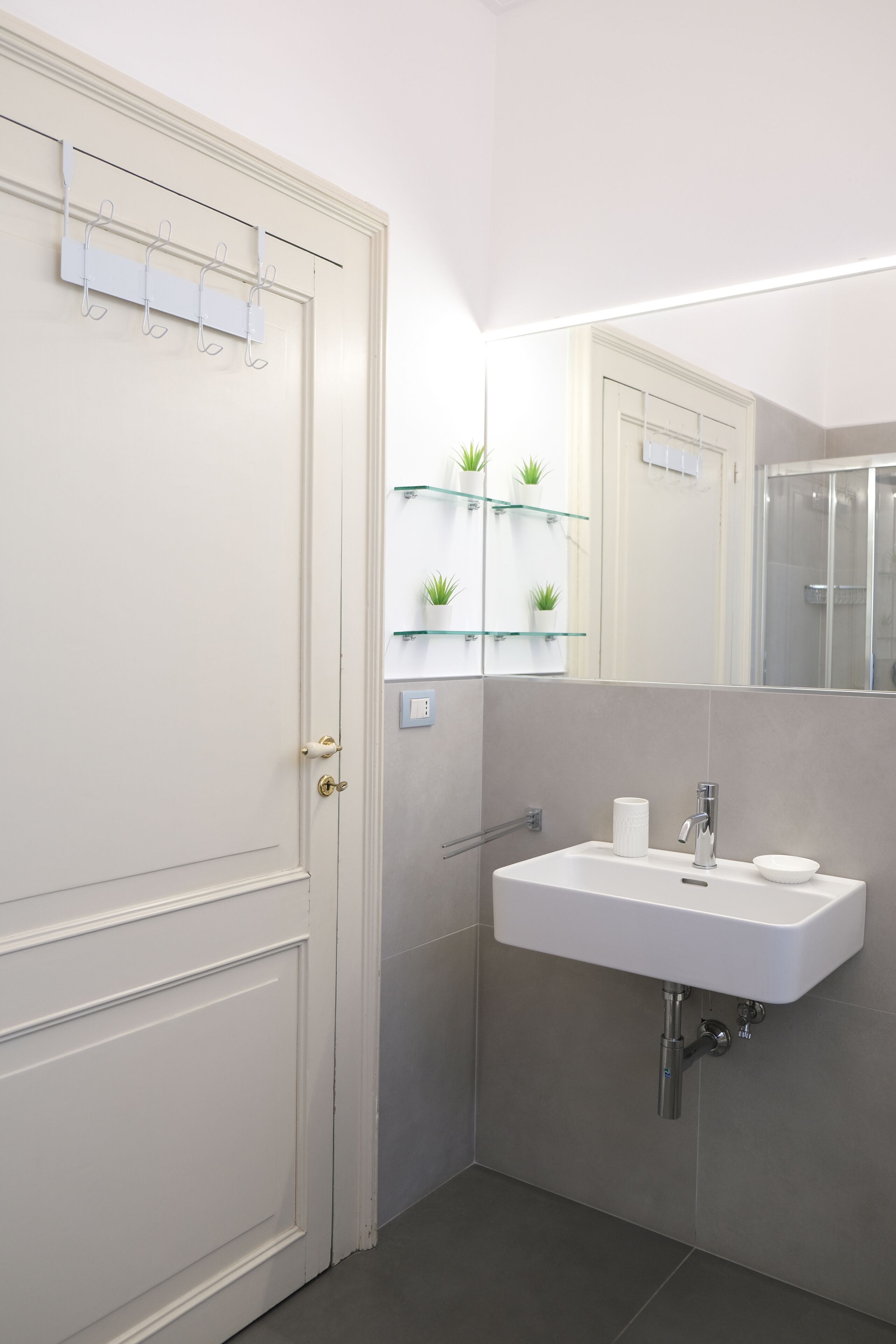A bathroom with a white sink, a mirror, and a door with a towel rack.