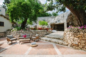 An outdoor patio with wicker furniture, a stone wall, and a tree providing shade. - Dimora Archimedea (Syracuse)
