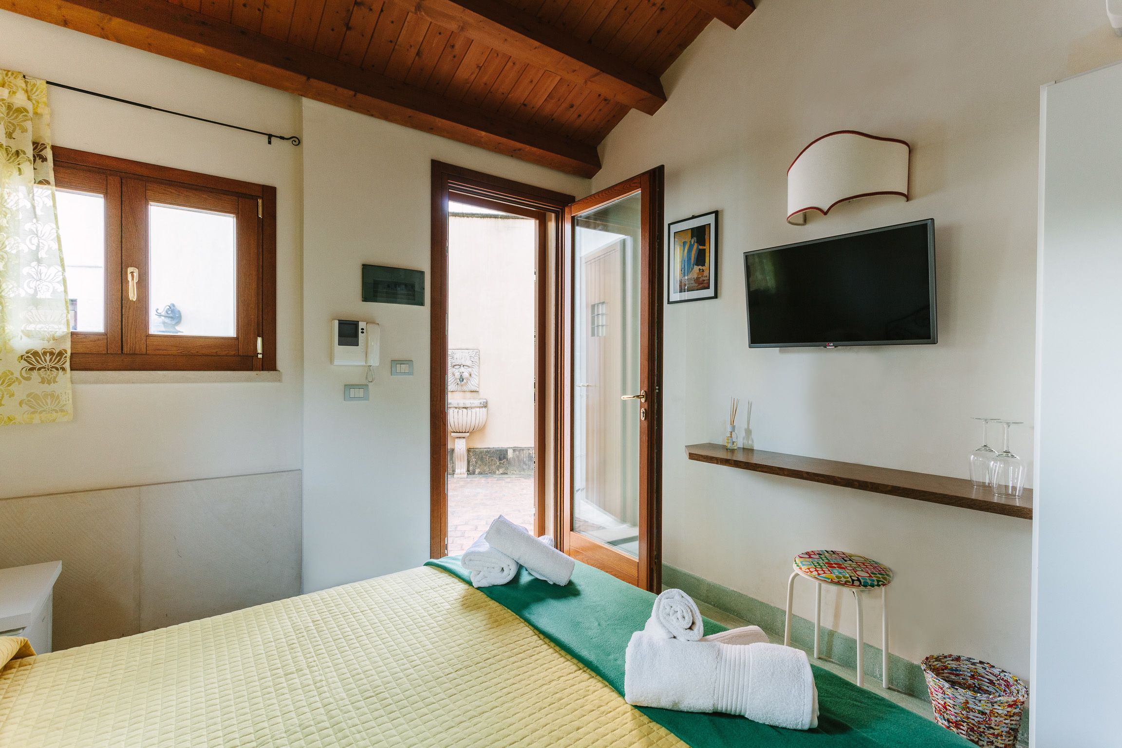 Habitación de hotel con cama, televisor, ventana y puerta que da a un área exterior.