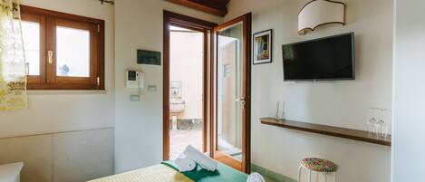 Habitación de hotel con cama, televisor, ventana y puerta que da a un área exterior.