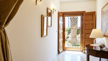 A hallway with a wooden door leading to an outdoor area, a wall-mounted mirror, and a table with a lamp.
