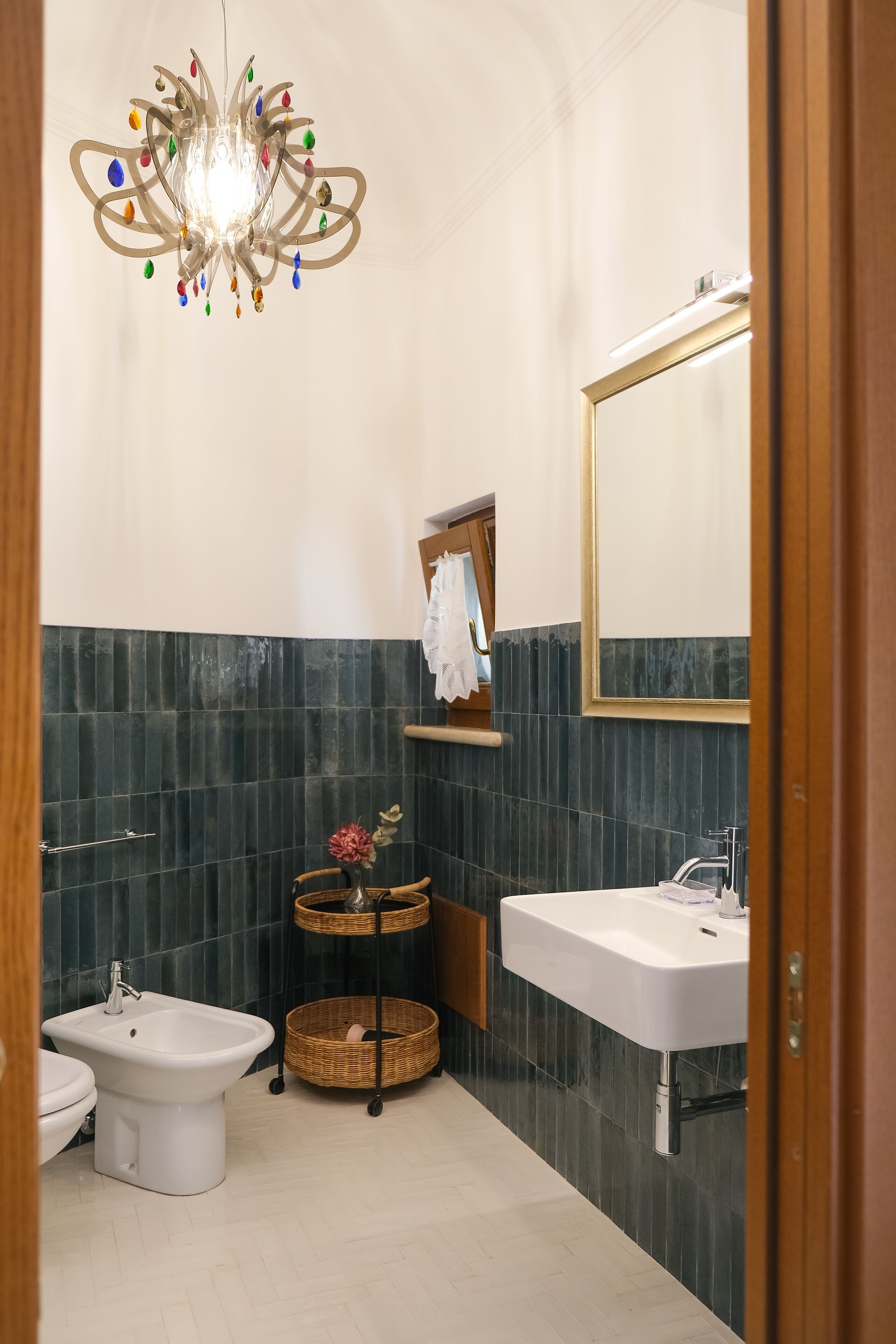 Un baño con bidé, lavamanos, espejo, candelabro y estante en la pared con una cesta.