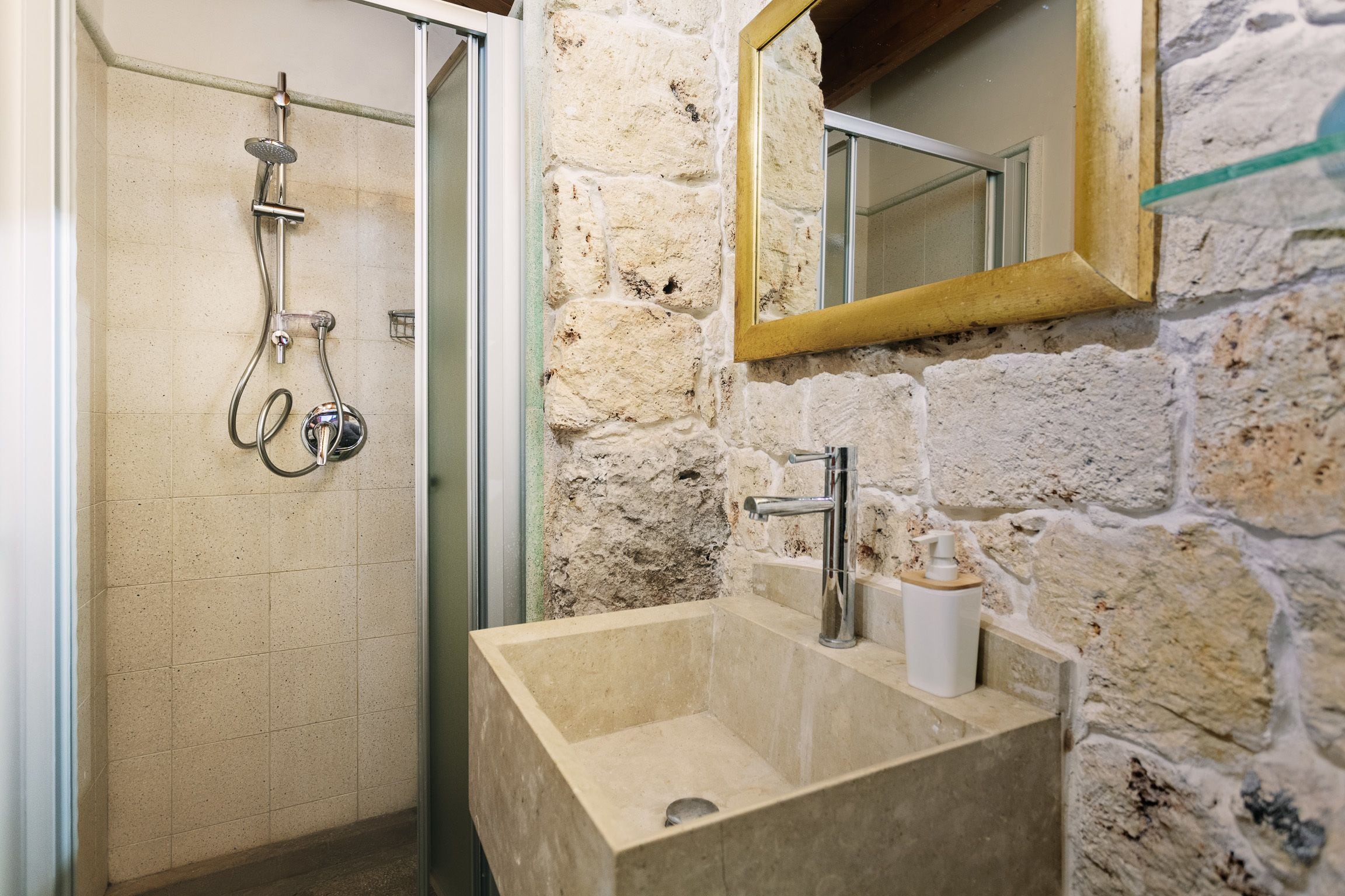 Een badkamer met een stenen muur, een wastafel met spiegel en een douche met handdouche.