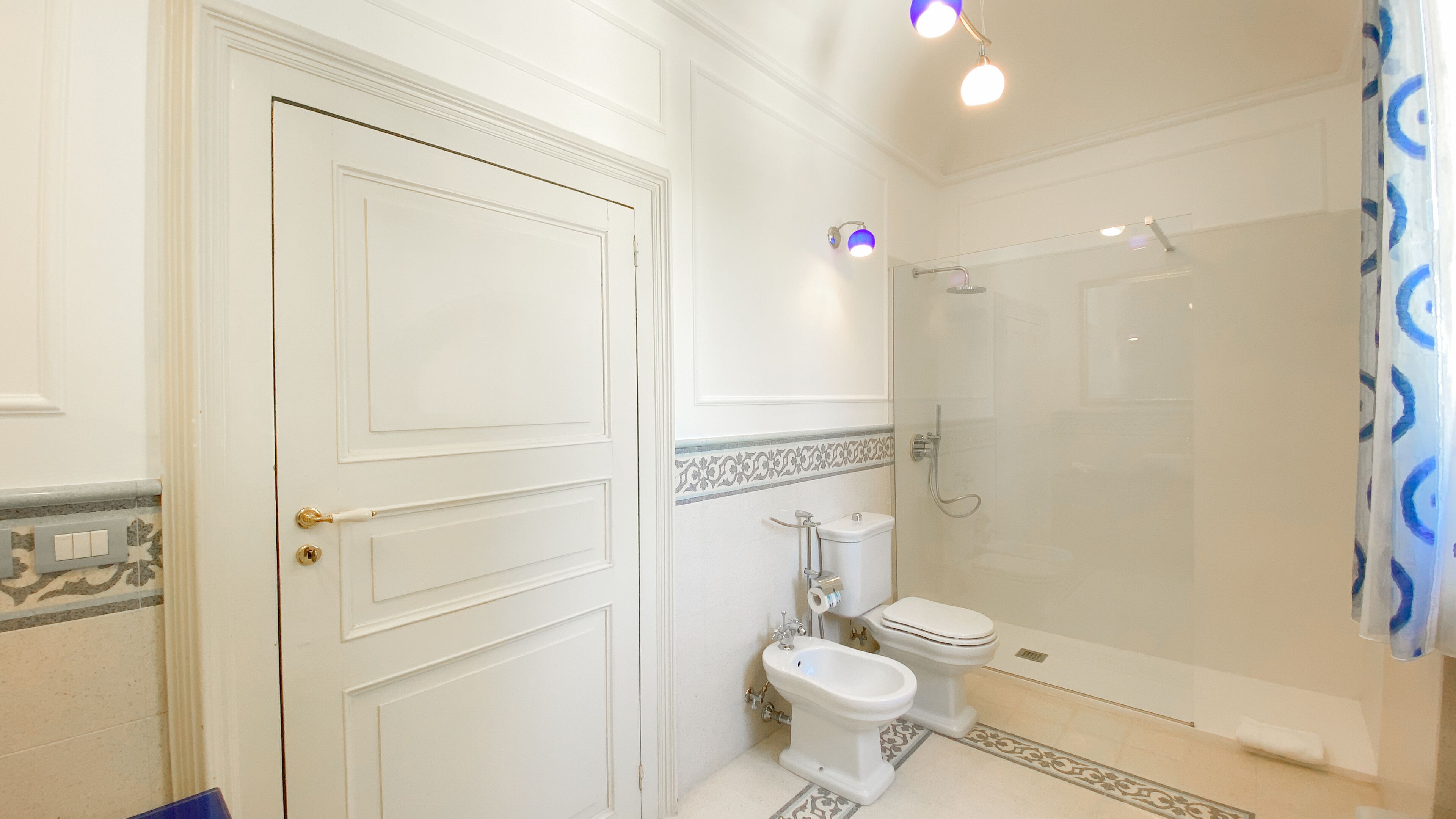 A bathroom with a white door, a toilet, a bidet, and a glass-enclosed shower.