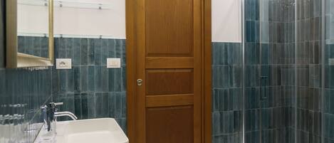 A bathroom with a wooden door, a white sink, and a glass shower enclosure.