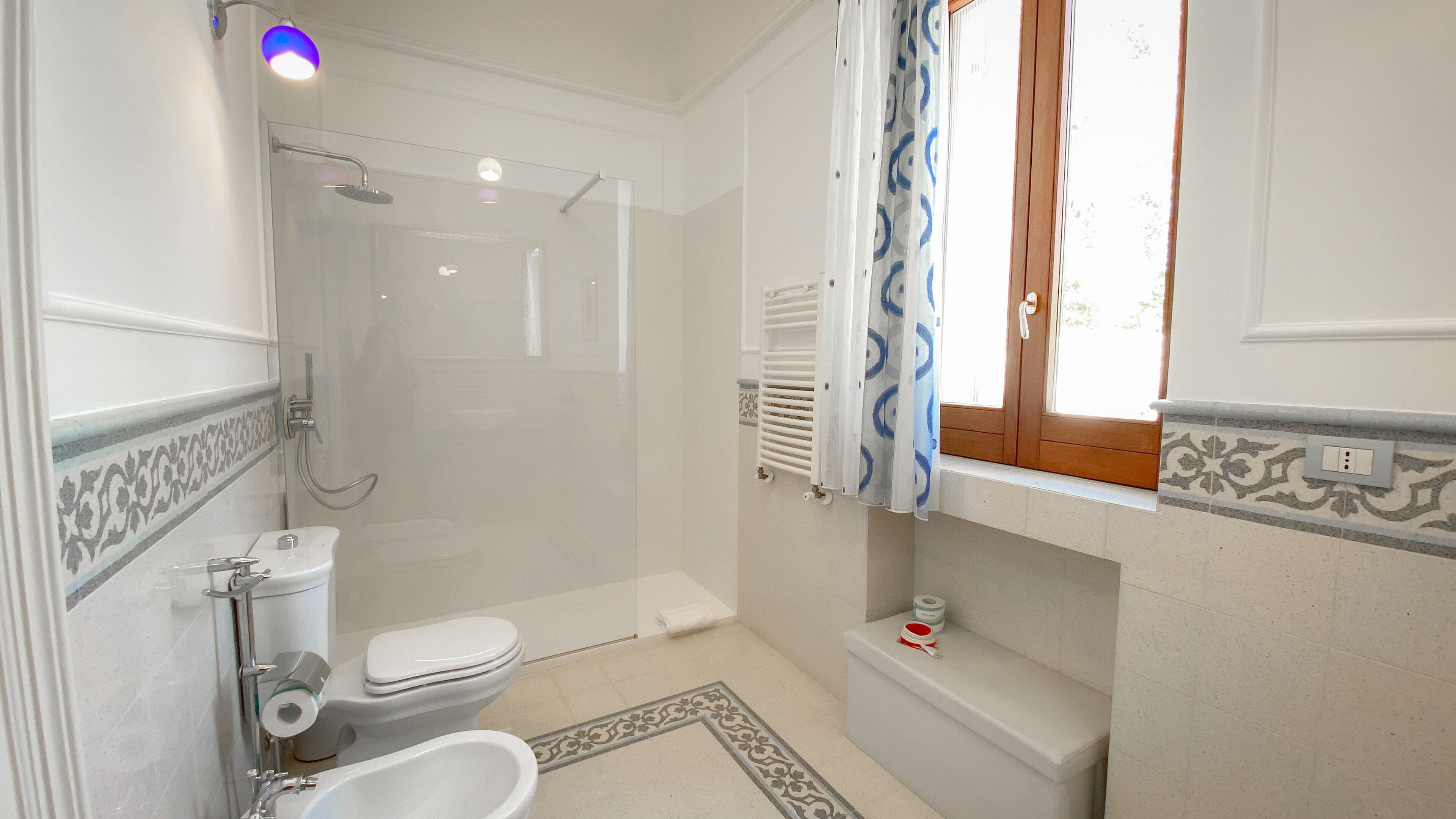 A bathroom with a shower, toilet, bidet, and a window with curtains.