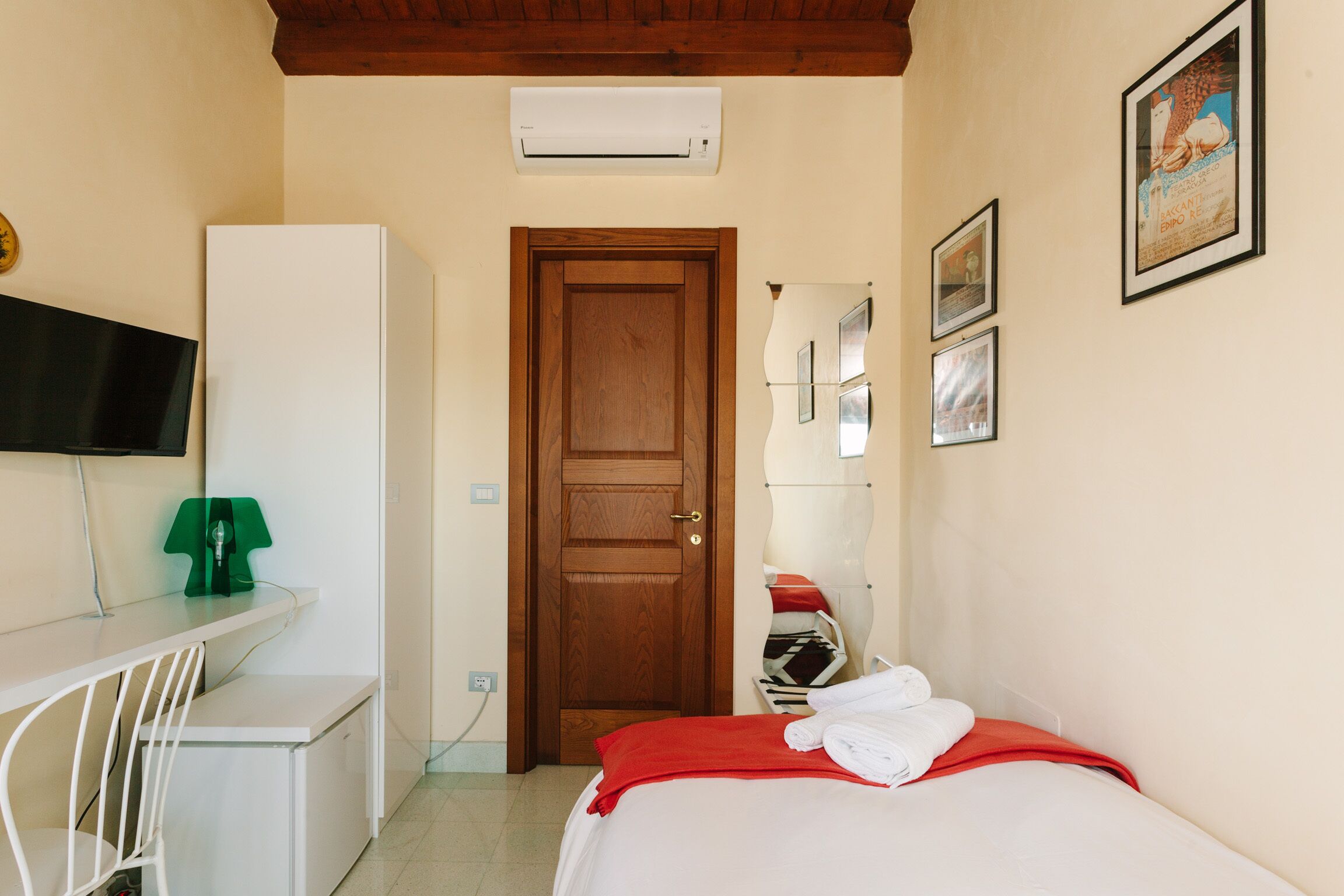 A hotel room with a bed, a desk, a chair, a television, and an air conditioning unit.
