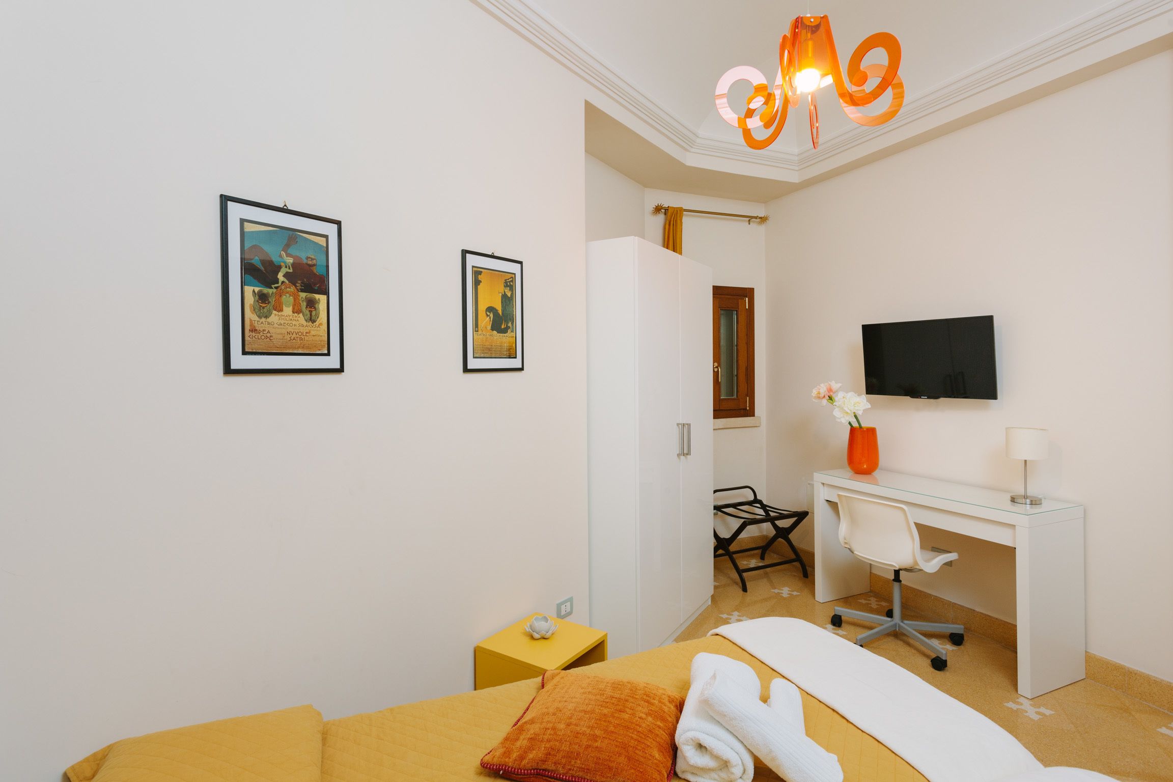 Habitación de hotel con una cama, un escritorio, una silla, un televisor y dos cuadros en la pared.