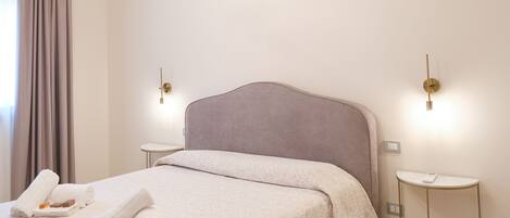 A neatly made bed with a grey headboard, a bedside table with a book, and a wall-mounted light fixture.