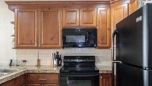 A kitchen with wooden cabinets, a black microwave, a black stove, and a black refrigerator.