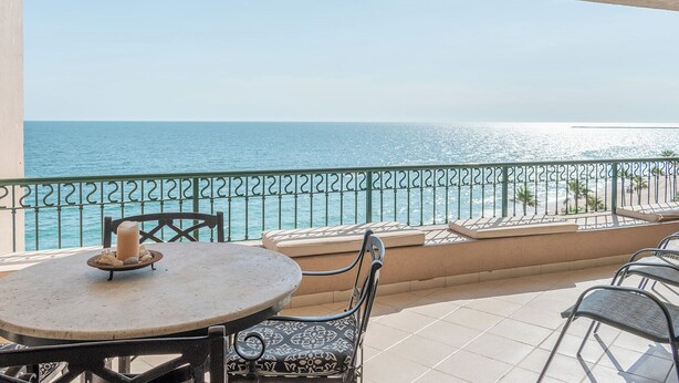 A balcony with a view of the sea, a table with a candle, and outdoor seating.