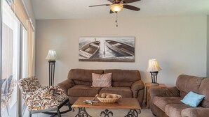 A living room with a brown sofa, a patterned armchair, a coffee table with decorative items, and a ceiling fan.