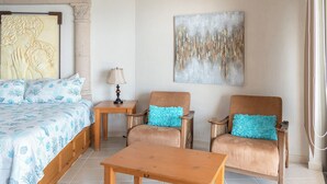 A bedroom with a bed, two armchairs, a table, a lamp, and a painting on the wall.