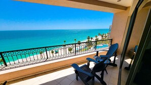 A balcony with a view of the ocean, a pool, and beach chairs.