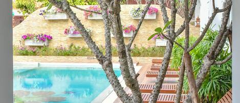 A view of a swimming pool surrounded by lush greenery and a stone wall with flower boxes.