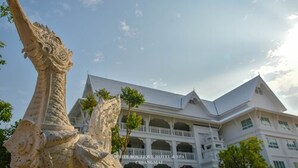 A large, ornate stone sculpture in front of a white building with multiple balconies and a clear sky. - White Boutique Hotel and Spa (Chiang Mai)