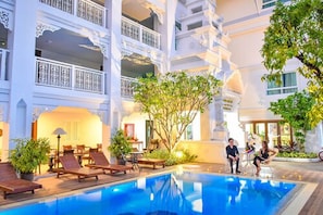 A hotel with a pool, outdoor seating, and a multi-story building with balconies.