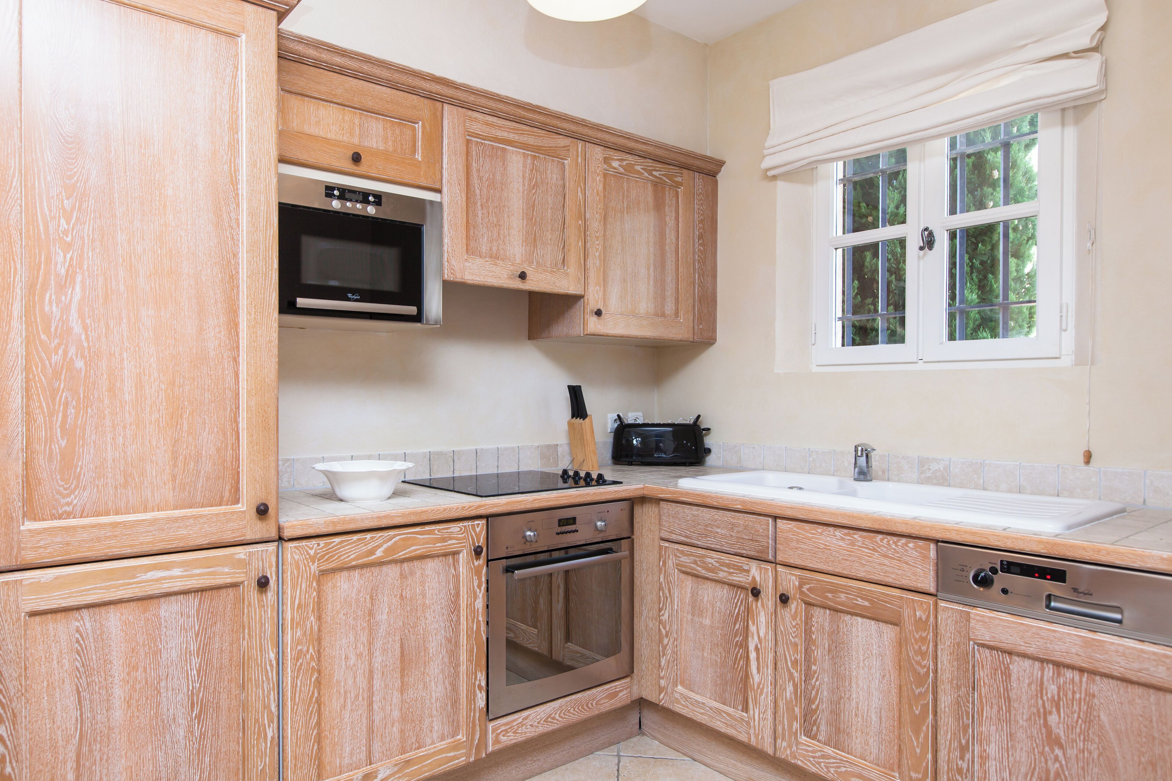 A kitchen with wooden cabinets, a microwave, stove, oven, and a window with curtains.