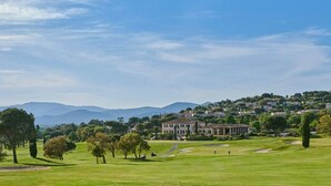 A golf course with a large building in the background, surrounded by trees and hills. - Golf Resort & Country Club Saint-Tropez (Gassin)