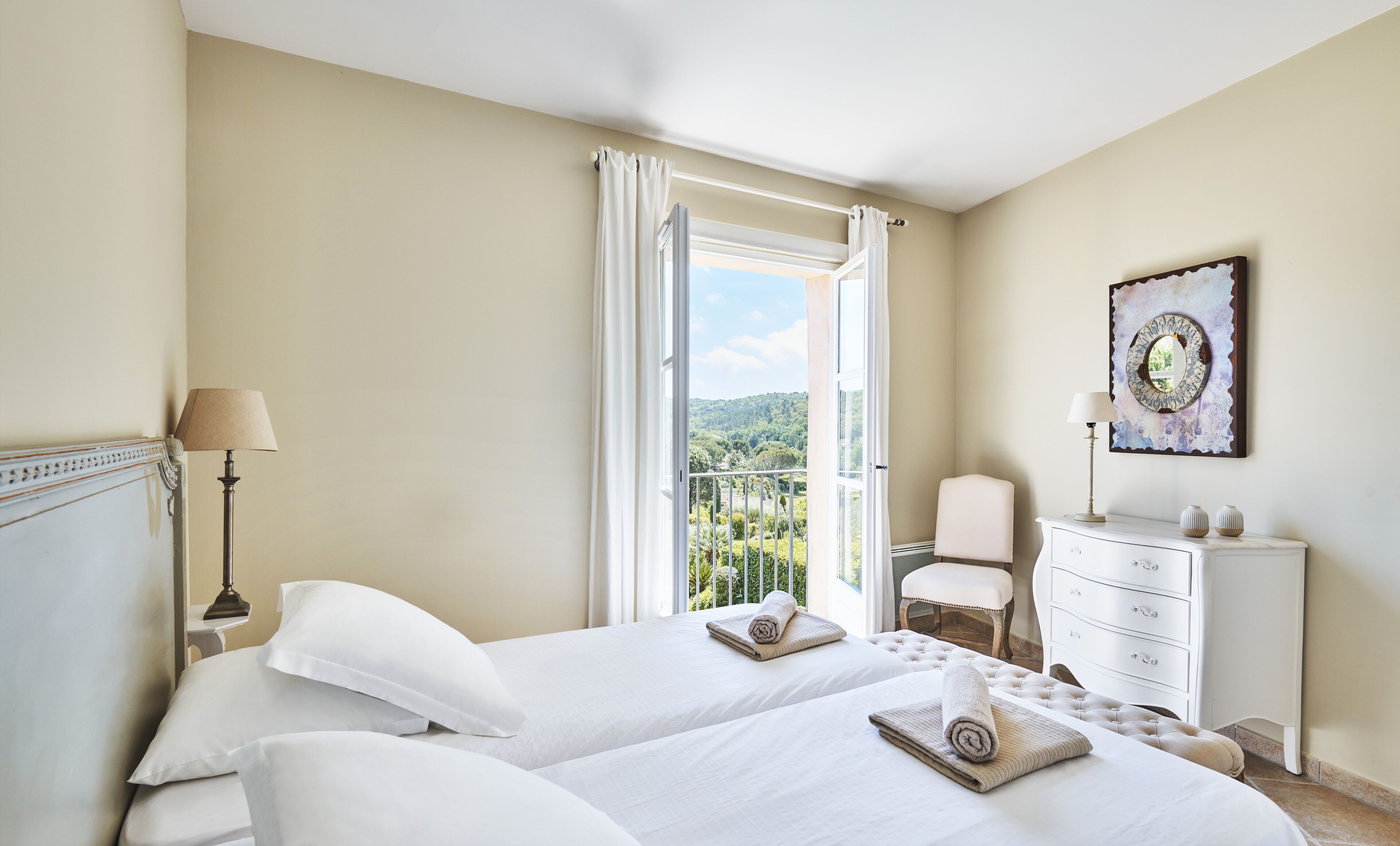 Une chambre d’hôtel avec deux lits, une chaise, une commode et une vue sur un balcon agrémenté de verdure.