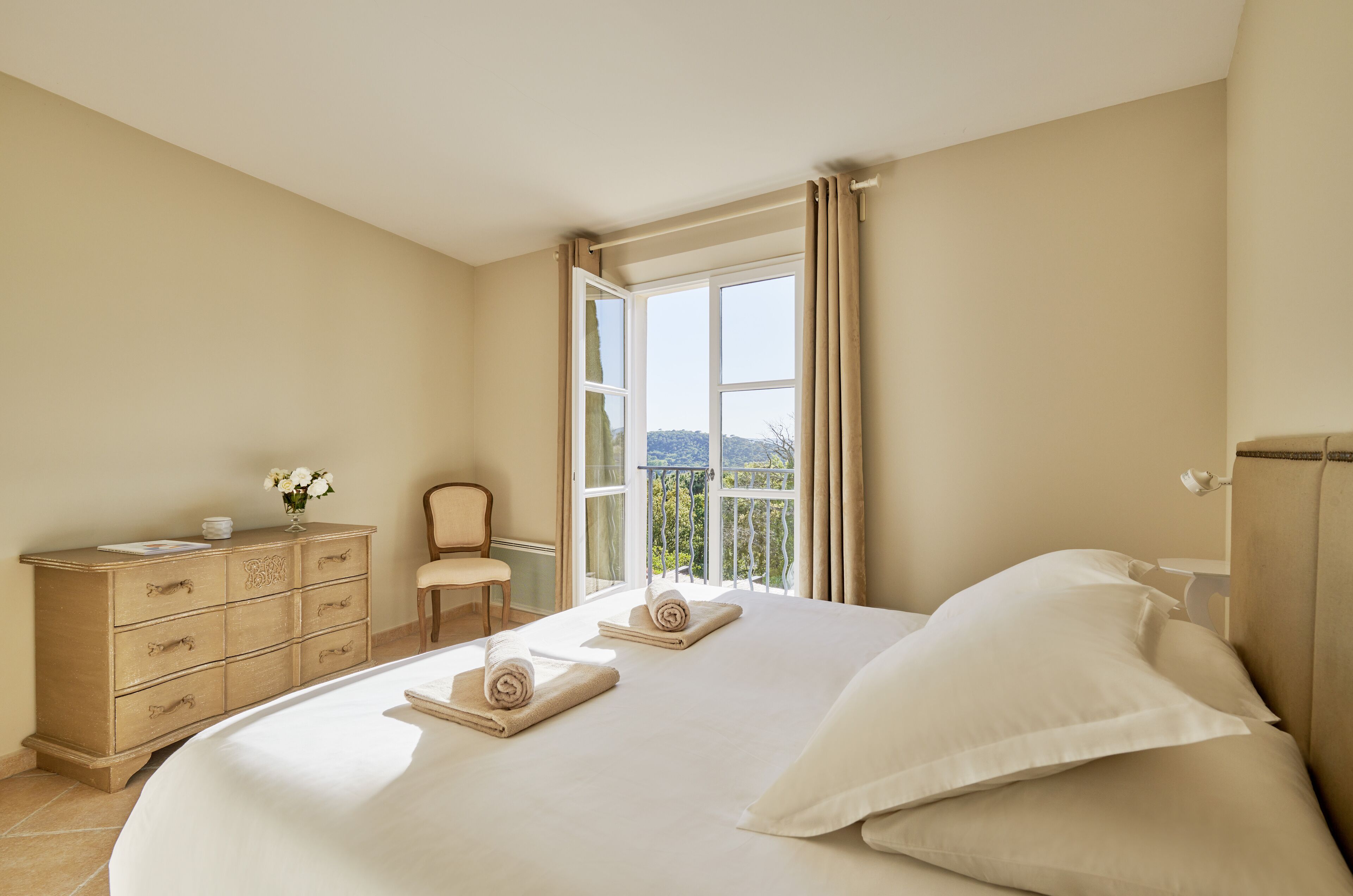 Un dormitorio con una cama grande, un aparador, una silla y un balcón con vistas.
