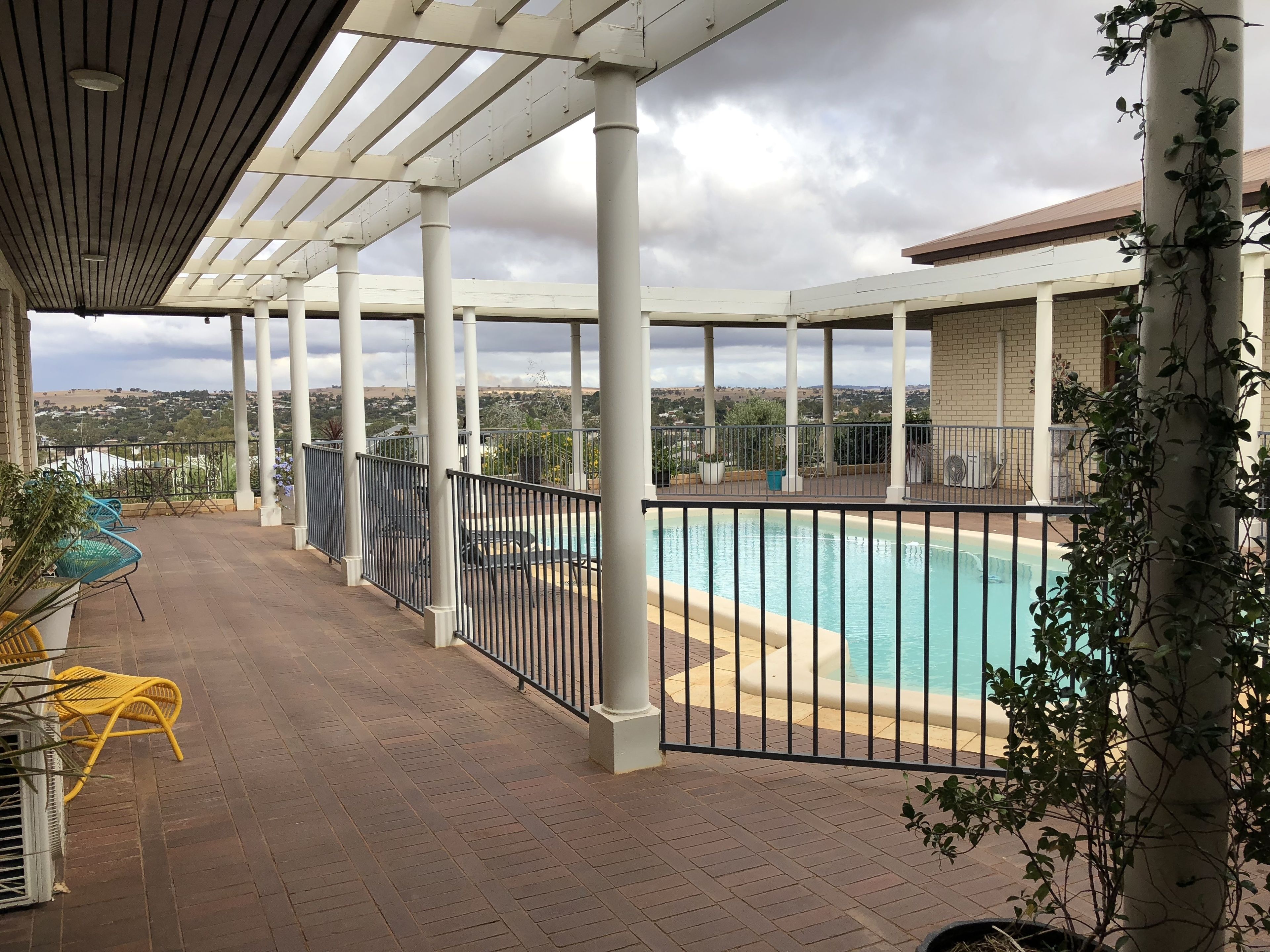 A covered outdoor area with a pool, seating, and a view of the landscape.
