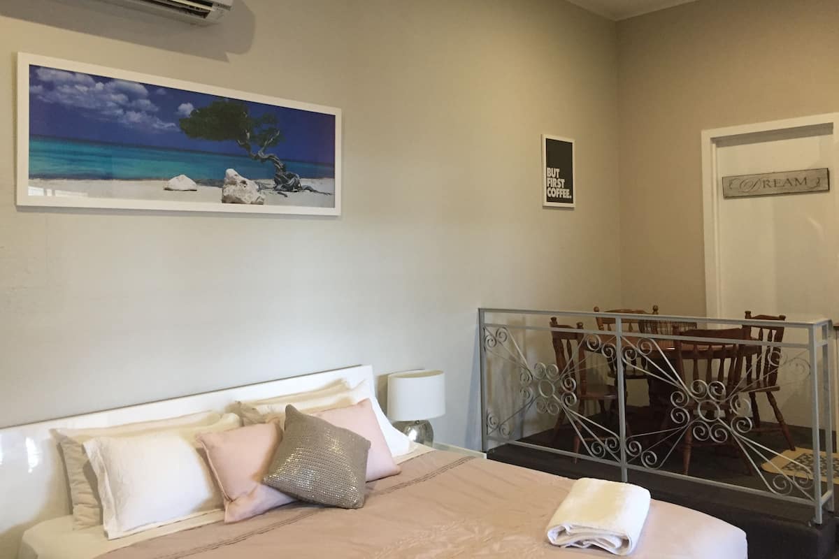Ein Hotelzimmer mit einem Bett, einem Bild von einer Strandansicht, einem Schild mit der Aufschrift "BUT FIRST COFFEE" und einer Tür mit der Bezeichnung "COFIREM".