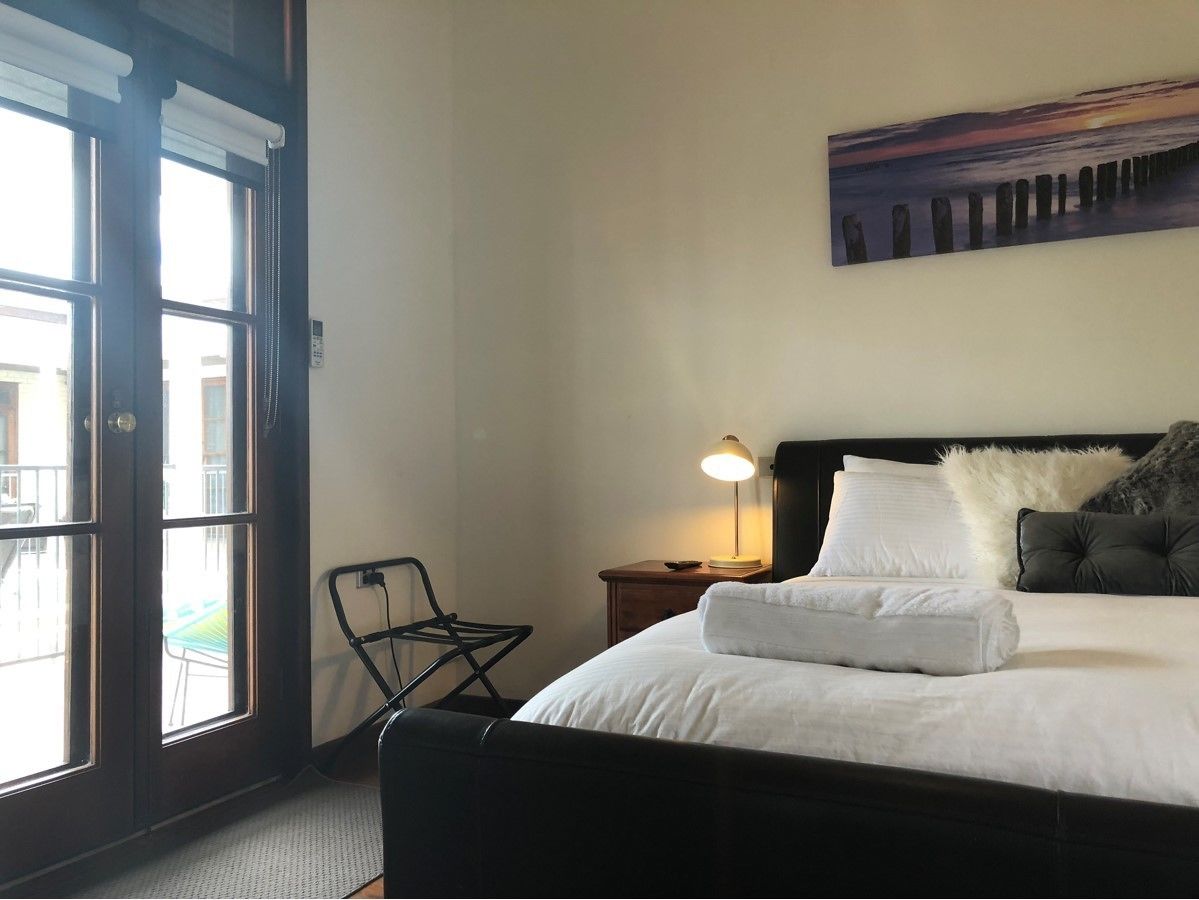 A hotel room with a bed, a nightstand, a lamp, a chair, and a painting on the wall.