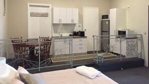 A hotel room with a bed, a dining table with chairs, a kitchen area with cabinets and appliances, and a balcony with a railing. - Fairway Manor Accommodation (Northam)