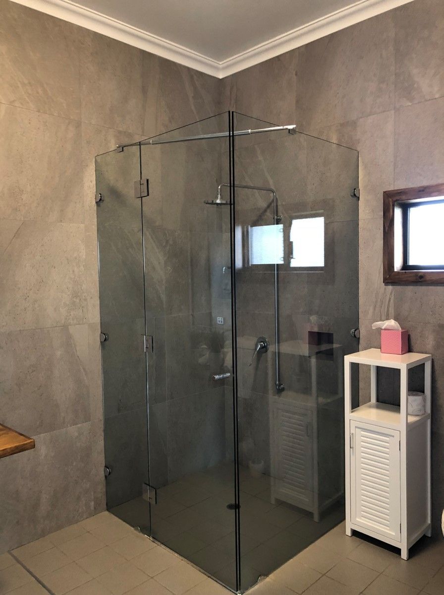 Ein modernes Badezimmer mit einer in Glas eingefassten Dusche, einem weißen Schrank mit Taschentuchbox und einem Spiegel an der Wand.