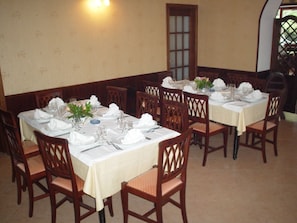 A dining area with tables set for four, wooden chairs, and a wall-mounted light fixture.