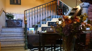 Un escalier avec un sol à carreaux, une table en bois surmontée d’un vase et un tableau accroché au mur.