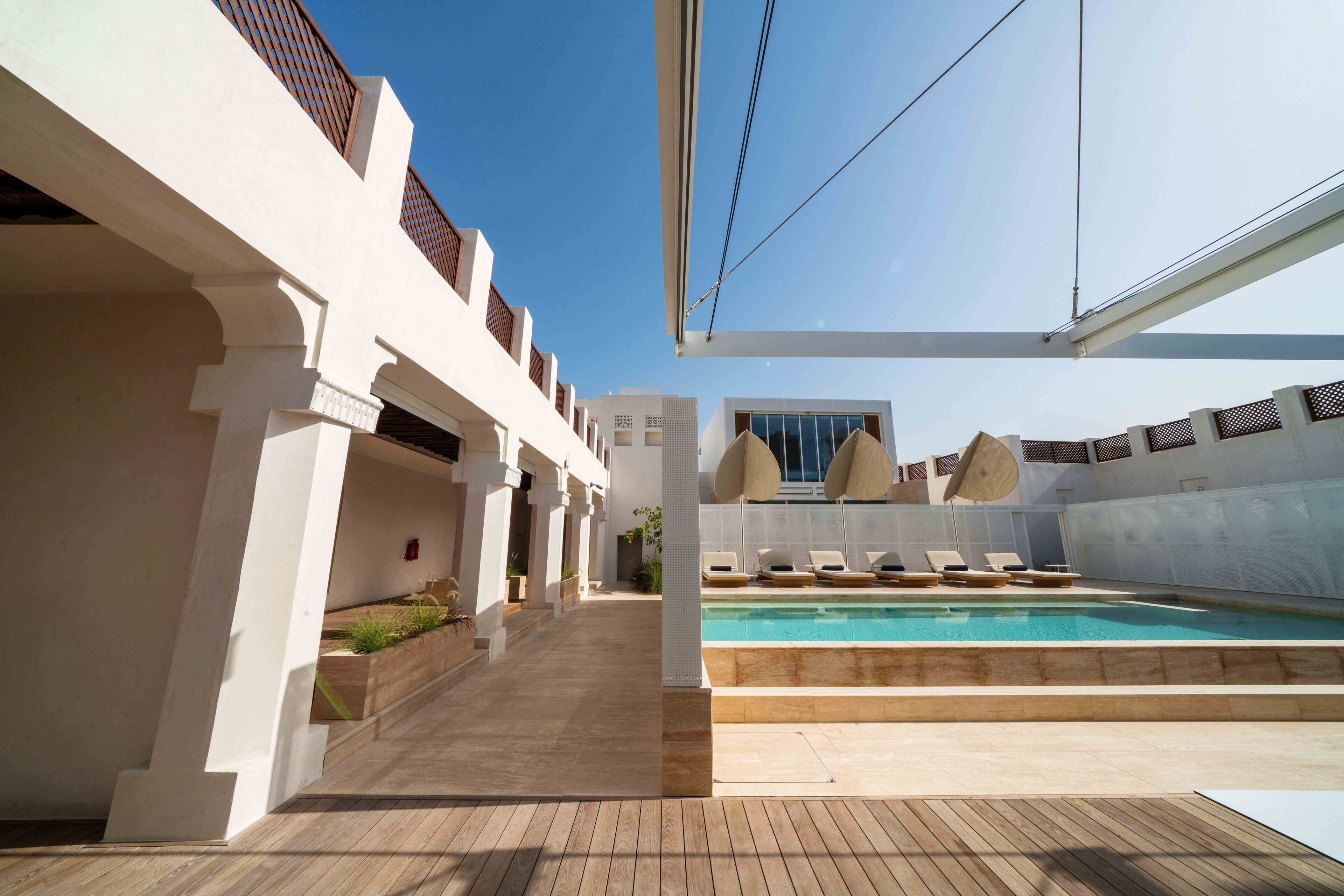 A modern outdoor pool area with a clear blue sky, a wooden deck, and lounge chairs.