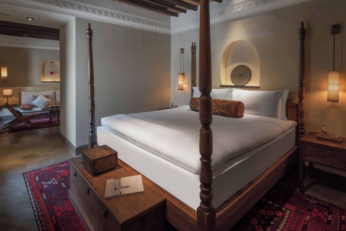 A four-poster bed with a wooden finish, a bedside table with a book and a glass, and a patterned rug on the floor.