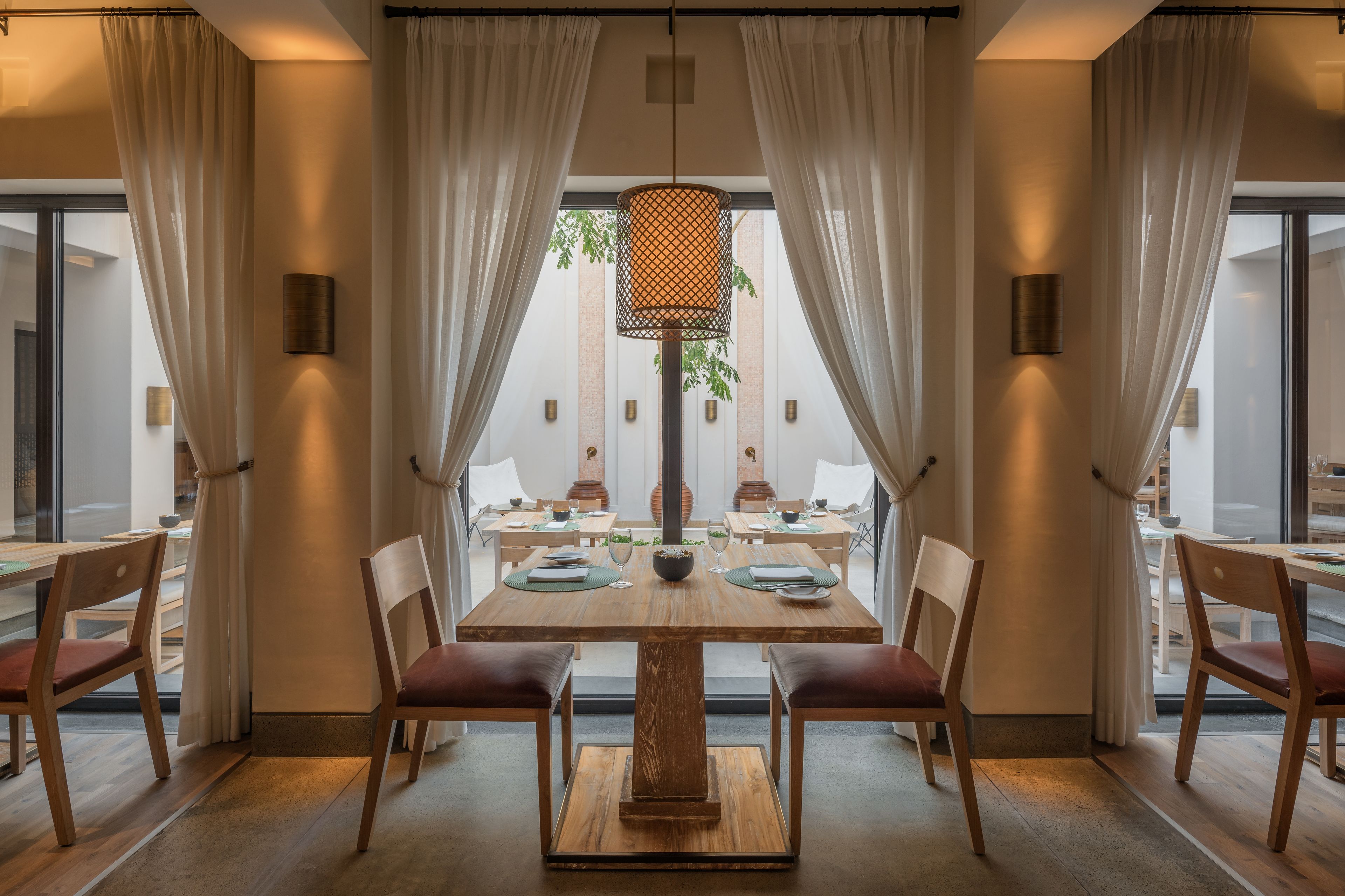 A dining area with a wooden table and chairs, a hanging light fixture, and curtains.