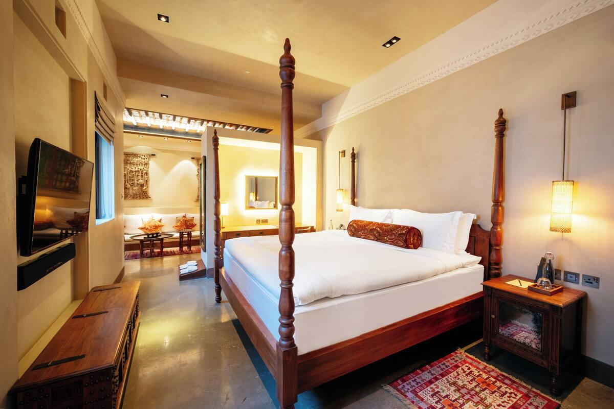 A four-poster bed with a wooden headboard, a bedside table with a lamp, and a television mounted on the wall.