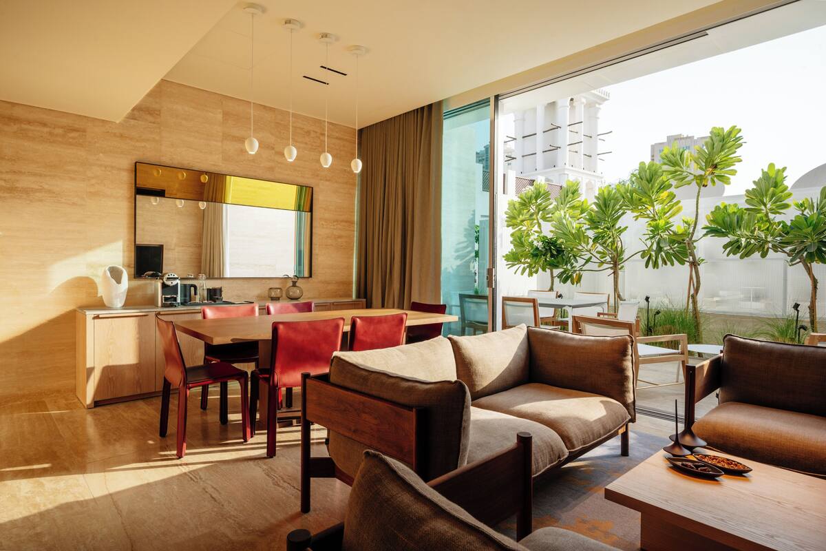 A modern hotel room with a dining area, a sofa set, and a large window with a view of the city.